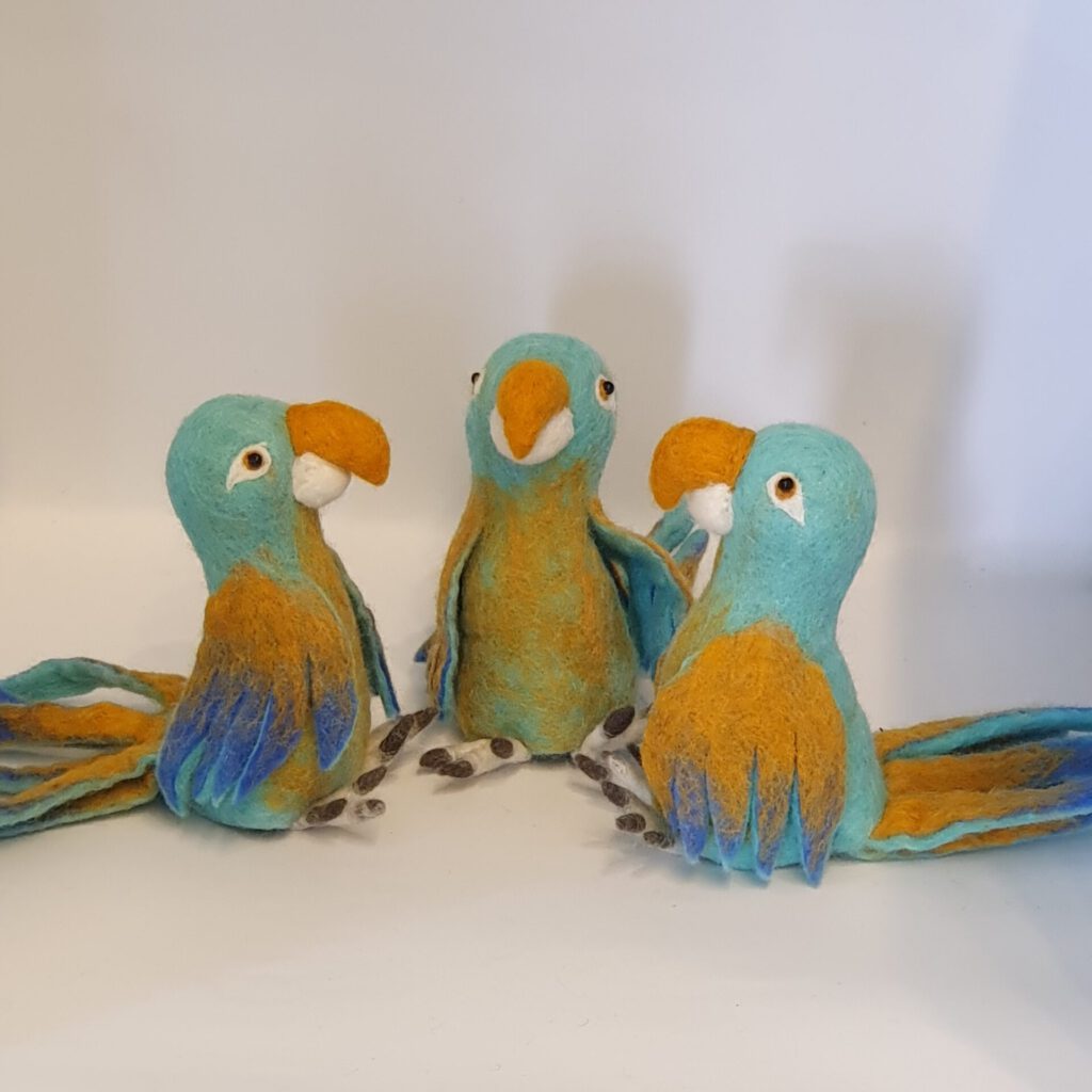 Drei bunte Papageien aus Filz mit blauen, grünen und orangen Farbtönen sitzen nebeneinander